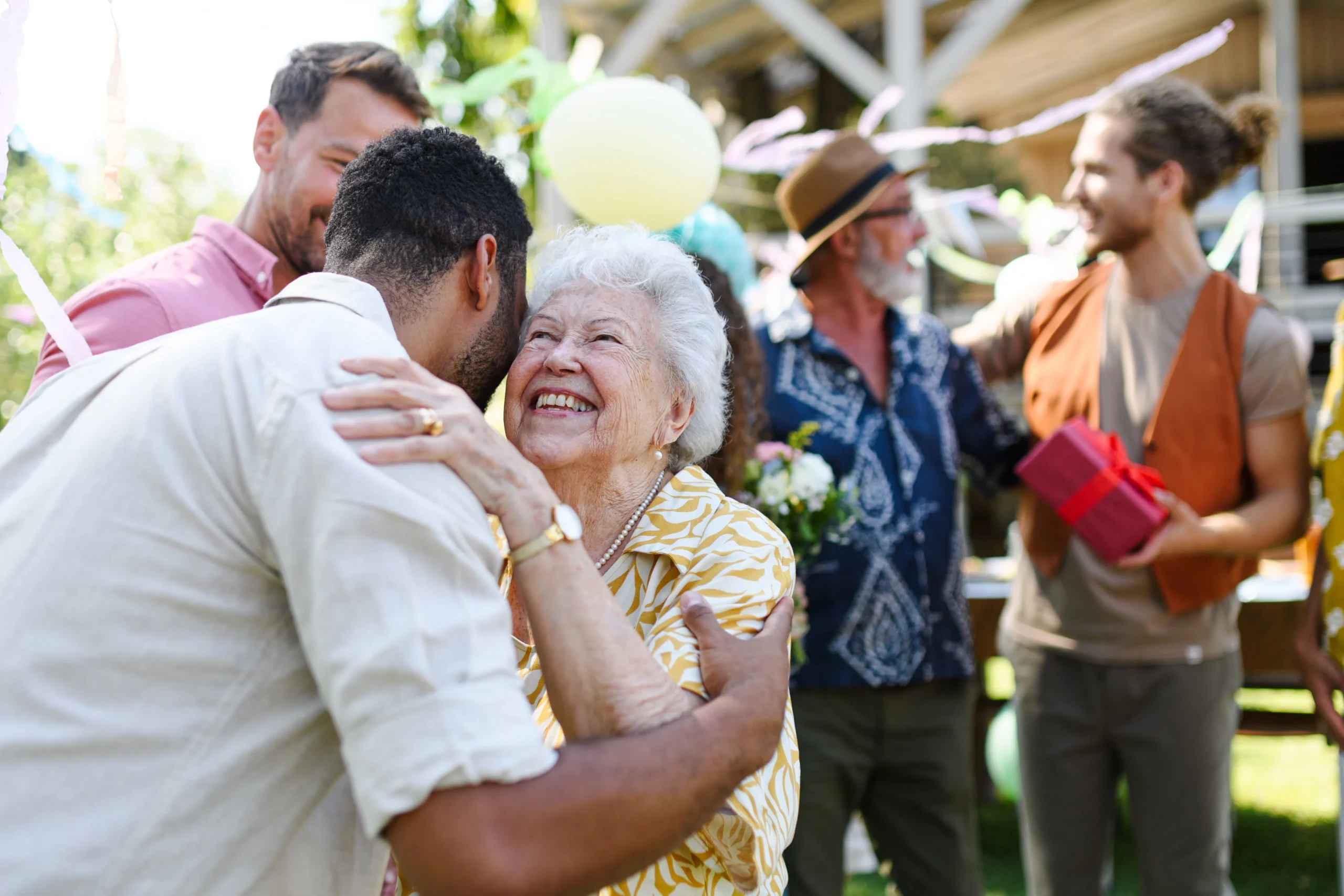 Elderly woman happily hugging her adult son during a family gathering, surrounded by loved