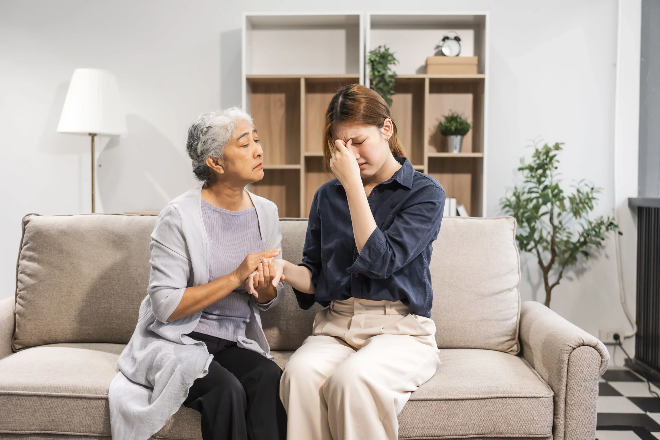 Daughter comforting her elderly mother at home, showing caregiver stress and emotional support.