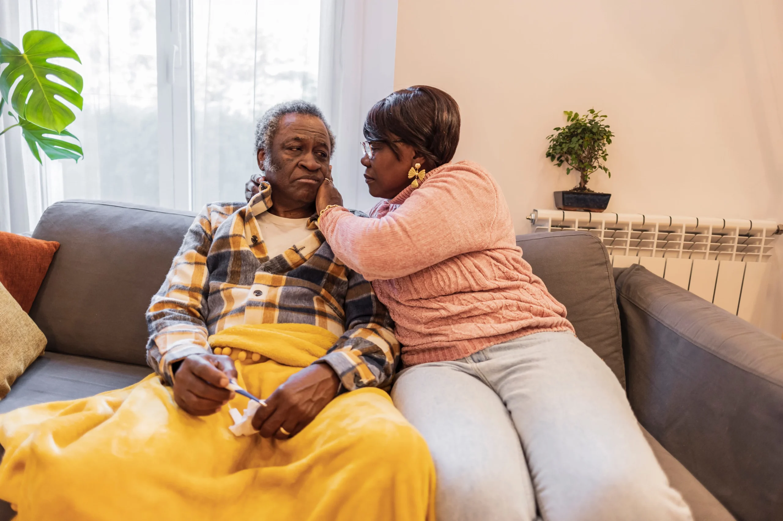 Daughter comforting her elderly father on the couch as he feels unwell, showing signs that additional home care may be needed.